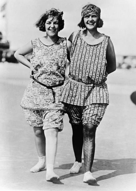 Two women are strolling along the beach in their swimming suits on - Old Photo